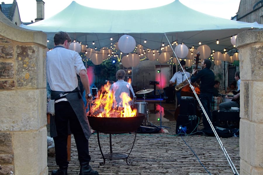 Cooking on a fire-pit Image of a stretch marquee with fire-pit cooking food