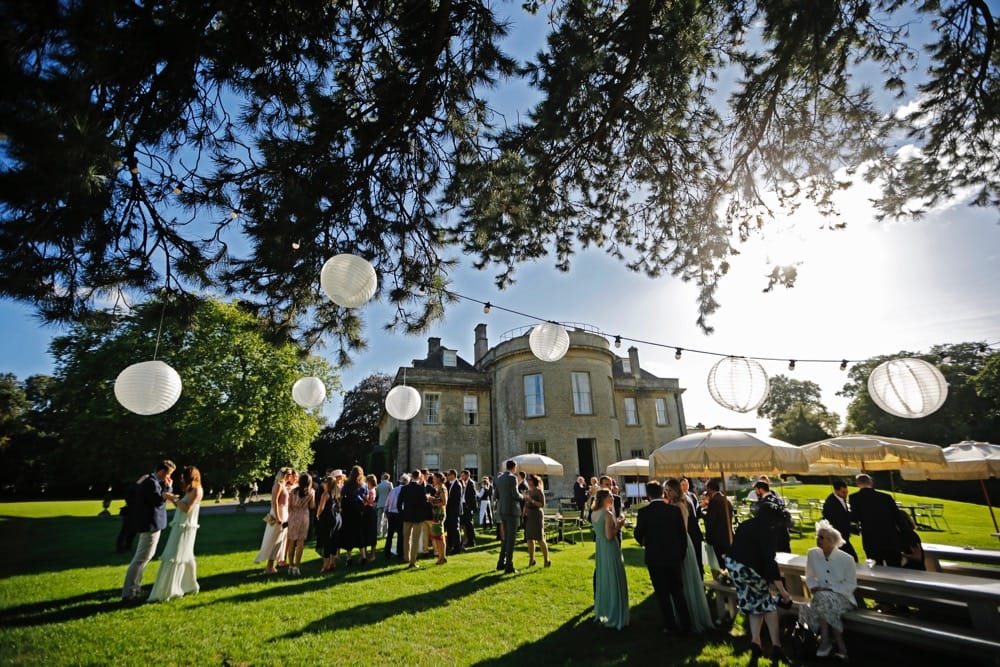 Image of Babington House in the summer with wedding guests and tree lighting.
